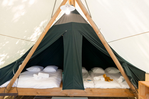 Intérieur d’une tente safari avec deux lits doubles, draps blancs, serviettes et une peluche sur le lit.