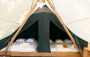 Interior of a safari tent featuring two double beds with white linens, towels, and a stuffed animal on bed.