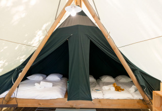 Binnenkant van een safaritent met twee dubbele bedden, witte lakens, handdoeken en een knuffel op bed.