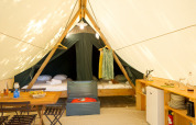 Interior view of a safari tent featuring a dining area, kitchenette, two beds, and sunlit ambiance.