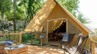 Safari tent with a wooden deck, lounge chairs, and cozy seating nestled in a lush forest camping site.