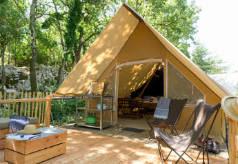 Safari tent with a wooden deck, lounge chairs, and cozy seating nestled in a lush forest camping site.