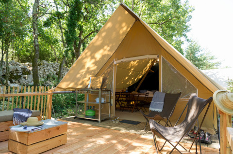 Safari-tent met houten terras en gezellige zithoek in het bos, perfect voor een comfortabele glamping.