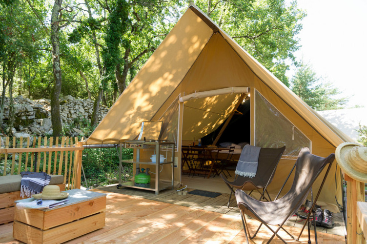 Safari tent with a wooden deck, lounge chairs, and cozy seating nestled in a lush forest camping site.