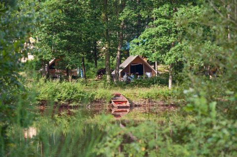 Safari-telt ved en sø omgivet af frodig skov, en lille robåd ligger forankret ved bredden om sommeren.