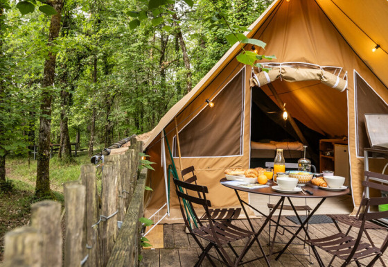 Safaritent in het bos met houten terras, gedekte buitentafel en een volledig uitgeruste campingkeuken.