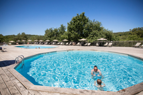 Zwei Schwimmbecken mit Liegestühlen und Sonnenschirmen im Village Huttopia Sud-Ardèche, Frankreich.