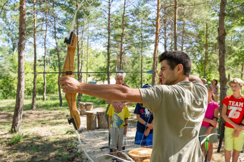 En mand lærer børn bueskydning i skoven ved Village Huttopia Sud-Ardèche, en feriepark i Frankrig.