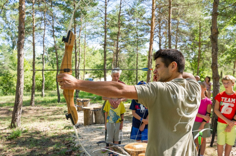 Un homme enseigne le tir à l’arc à des enfants dans la forêt du Village Huttopia Sud-Ardèche en France.