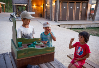 Tre børn leger med et udendørs spil på en bænk ved Village Huttopia Sud-Ardèche feriepark i Frankrig.