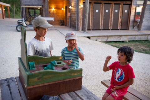 Tre bambini giocano con un gioco all'aperto su una panchina al Village Huttopia Sud-Ardèche in Francia.
