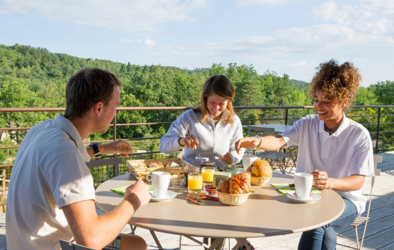 Trois personnes prennent le petit-déjeuner en terrasse avec vue sur la nature à Village Huttopia Sud-Ardèche.
