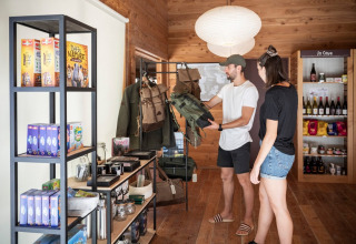 Two people look at outdoor gear in a shop at Village Huttopia Sud-Ardèche, France, with shelves of products.