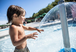 Ein Kind spielt am Wasserpilz im Schwimmbadbereich von Village Huttopia Sud-Ardèche, Auvergne-Rhône-Alpes.