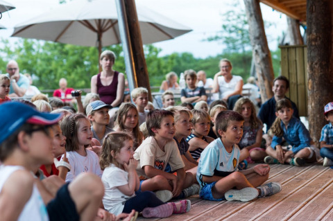 Niños atentos disfrutan de un espectáculo al aire libre en Village Huttopia Sud-Ardèche, parque vacacional en Francia.