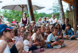 Des enfants assistent attentivement à un spectacle en plein air au Village Huttopia Sud-Ardèche, en France.
