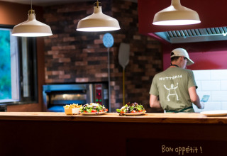 A chef prepares food in an open kitchen with fresh salads on the counter at Village Huttopia Sud-Ardèche.
