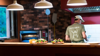 A chef prepares food in an open kitchen with fresh salads on the counter at Village Huttopia Sud-Ardèche.