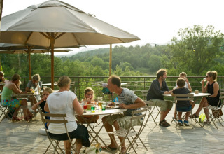 Menschen sitzen entspannt auf einer Terrasse im Grünen im Village Huttopia Sud-Ardèche in Frankreich.