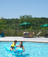 Eine Mutter und ein Kind spielen im Außenpool mit einem blauen aufblasbaren Delfin im Huttopia Sud-Ardèche.