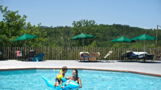 A mother and child play with a blue inflatable dolphin in the outdoor pool at Huttopia Sud-Ardèche holiday park.