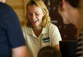 Receptionist smiler og hjælper gæster på Village Huttopia Sud-Ardèche feriested i Auvergne-Rhône-Alpes, Frankrig.