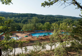 Luftaufnahme eines Schwimmbads mit Sonnenschirmen im Ferienpark Huttopia Sud-Ardèche, Auvergne-Rhône-Alpes.