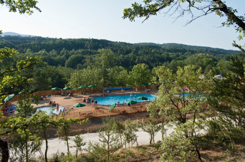 Luftaufnahme eines Schwimmbads mit Sonnenschirmen im Ferienpark Huttopia Sud-Ardèche, Auvergne-Rhône-Alpes.