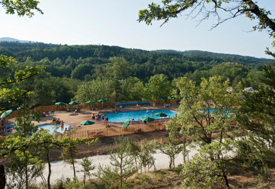 Aerial view of swimming pools and green umbrellas at Village Huttopia Sud-Ardèche, Auvergne-Rhône-Alpes, France.