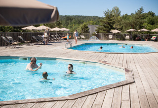 Ferieparkgæster nyder to udendørs swimmingpools med liggestole og parasoller i det solrige Sud-Ardèche.