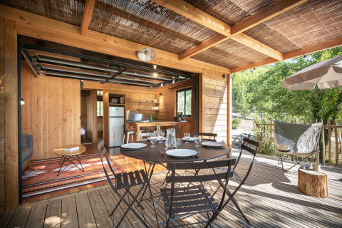 Zona de comedor exterior con mesa puesta y cocina abierta en una cabaña de Village Huttopia Sud-Ardèche, Francia.