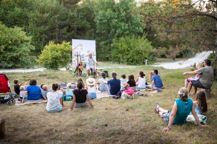 Des familles assises sur des couvertures écoutent un conteur à Village Huttopia Sud-Ardèche en France.