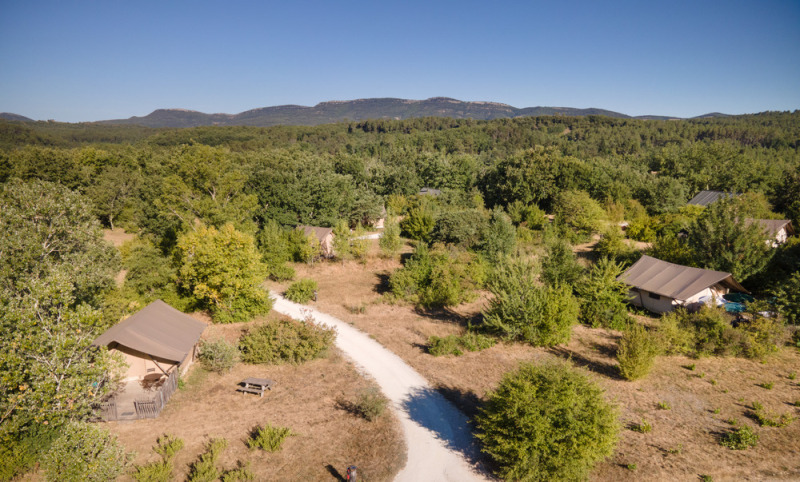 Vue aérienne du Village Huttopia Sud-Ardèche avec tentes, sentier blanc et végétation en Auvergne-Rhône-Alpes.