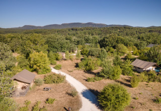 Vue aérienne du Village Huttopia Sud-Ardèche avec tentes, sentier blanc et végétation en Auvergne-Rhône-Alpes.