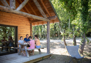 Familie nyder et måltid udenfor en træhytte i skoven i Village Huttopia Sud-Ardèche, Auvergne-Rhône-Alpes.