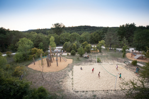 Kinder spielen Volleyball auf einem Sandplatz und genießen den Spielplatz im Village Huttopia Sud-Ardèche.