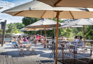 Terraza al aire libre con sombrillas y huéspedes en Village Huttopia Sud-Ardèche, Auvergne-Rhône-Alpes, Francia.