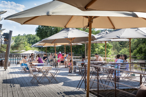 Terrasse extérieure avec parasols et visiteurs au Village Huttopia Sud-Ardèche en Auvergne-Rhône-Alpes, France.