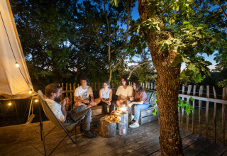 En gruppe mennesker sidder og hygger sig på en terrasse om aftenen i Village Huttopia Sud-Ardèche, Frankrig.