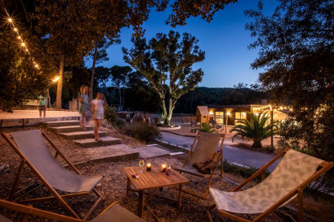 Ambiente nocturno en Huttopia La Forêt de Janas, Provence-Alpes-Côte d’Azur, Francia, con sillas y luces decorativas.