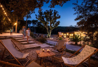 Avondbeeld bij Huttopia La Forêt de Janas, Provence-Alpes-Côte d’Azur, met relaxstoelen en gezellige verlichting.