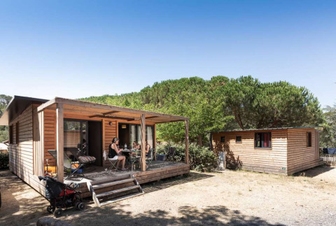 Visitantes disfrutan al aire libre en cabañas de madera en Huttopia La Forêt de Janas, Provenza, Francia.