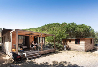 Visitantes disfrutan al aire libre en cabañas de madera en Huttopia La Forêt de Janas, Provenza, Francia.
