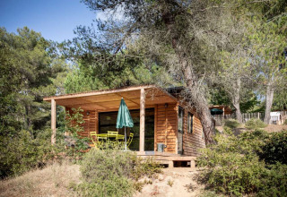 Een houten chalet met overdekt terras en tuinset tussen de bomen in Huttopia La Forêt de Janas in de natuur.