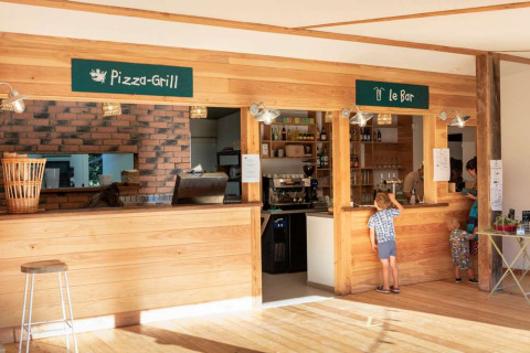 Imagen de la zona de pizza-grill y bar en Huttopia La Forêt de Janas, parque vacacional de Provenza-Alpes-Costa Azul, Francia.