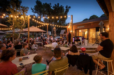 Evento al aire libre por la tarde con familias y niños bajo luces en Huttopia La Forêt de Janas, Provenza.