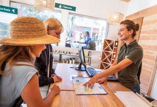 Twee vrouwen krijgen informatie van een receptioniste met een kaart in Huttopia La Forêt de Janas, Frankrijk.