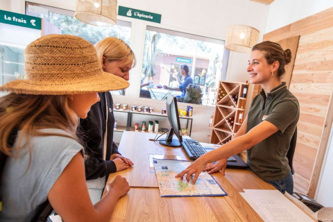 Zwei Frauen erhalten Karteninformationen von einer freundlichen Rezeptionistin im Huttopia La Forêt de Janas, Frankreich.
