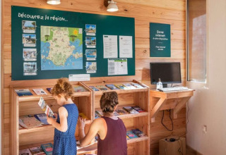 Une mère et sa fille découvrent des brochures à Huttopia La Forêt de Janas, un parc de vacances en France.