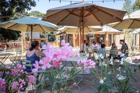 Outdoor café area with sun umbrellas and flowers at Huttopia La Forêt de Janas holiday park in southern France.